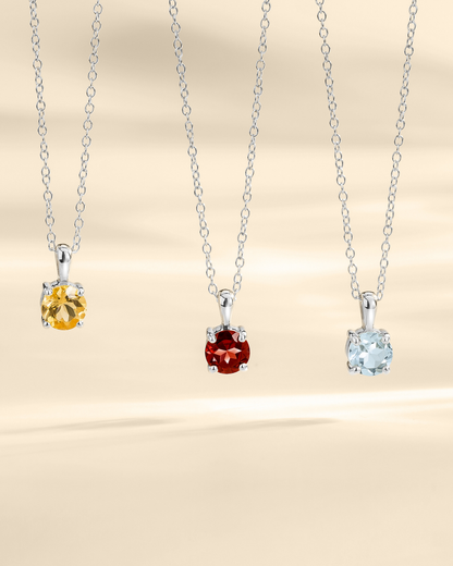Three silver pendants with different colored gemstones on a beige background