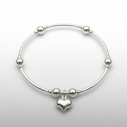 Silver bracelet with a puff heart charm on a light gray background