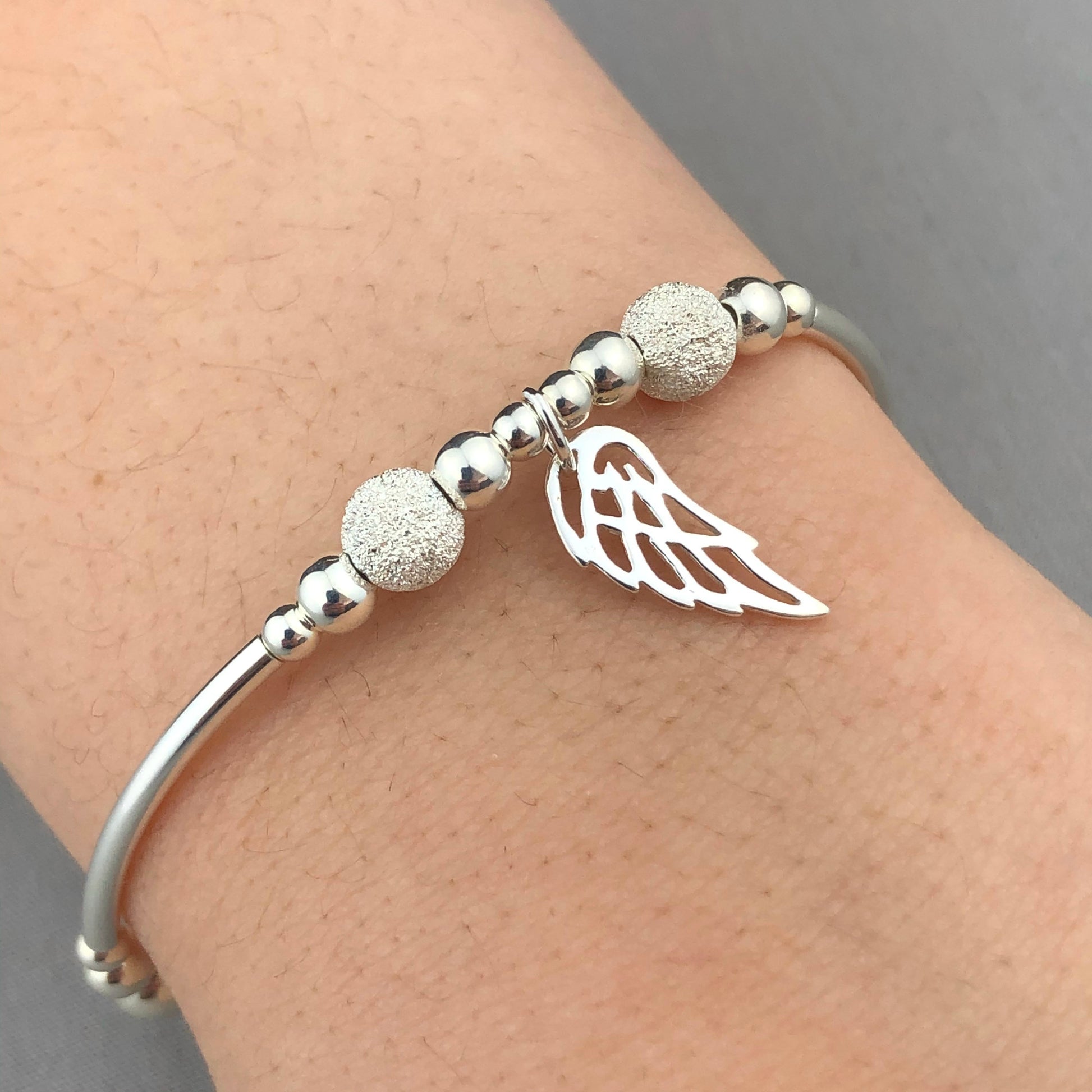 Model closeup of angel wing charm women's sterling silver stacking bracelet by My Silver Wish